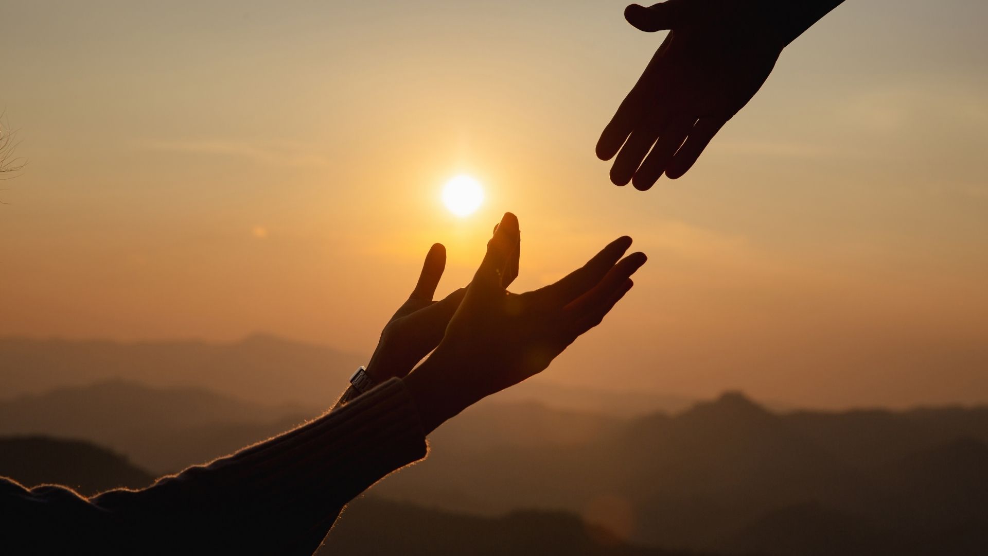 two hands extended to each other at sunset