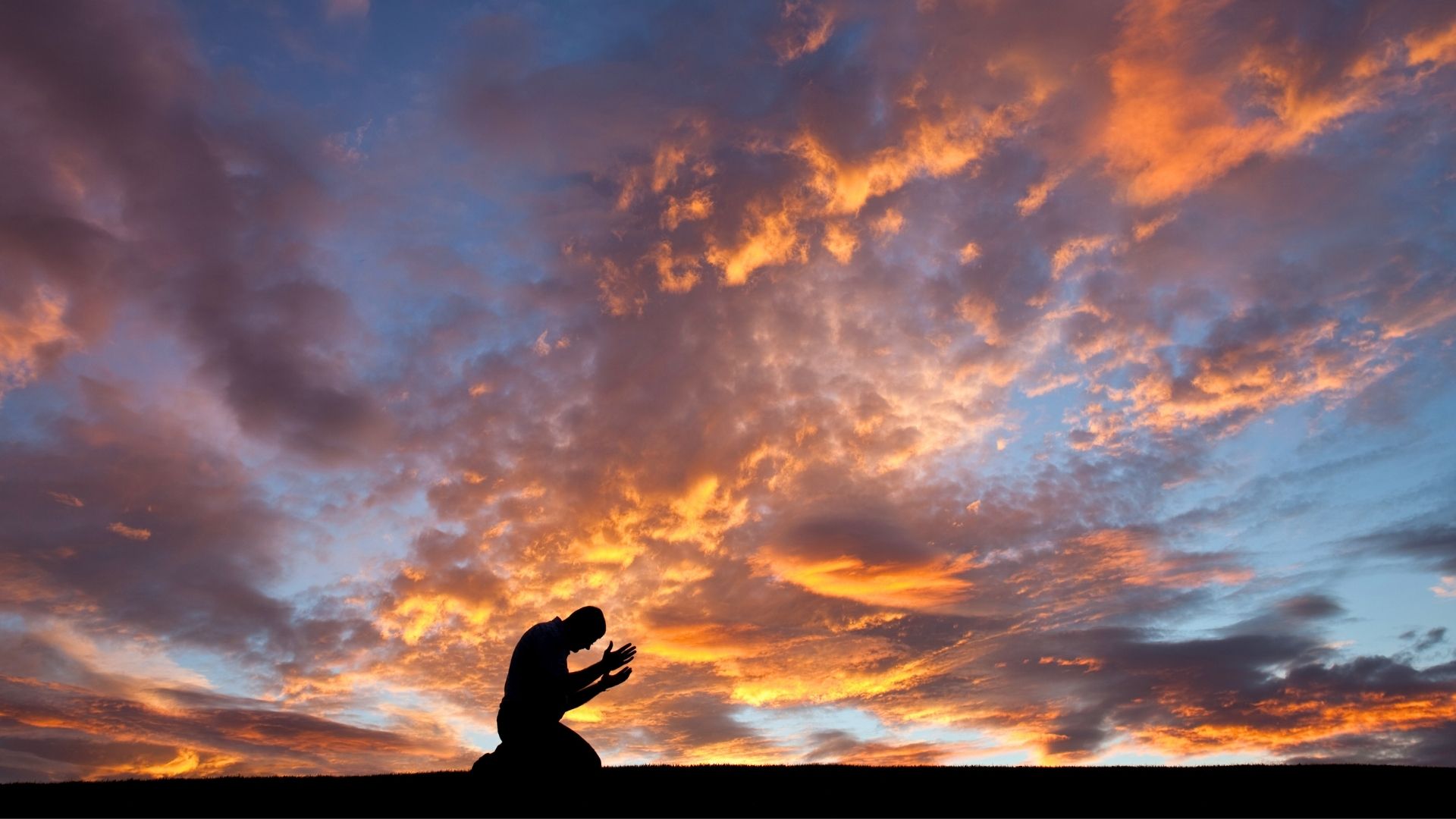 man praying with hands up to sky of blue orange and pink sunset landscape backdrop