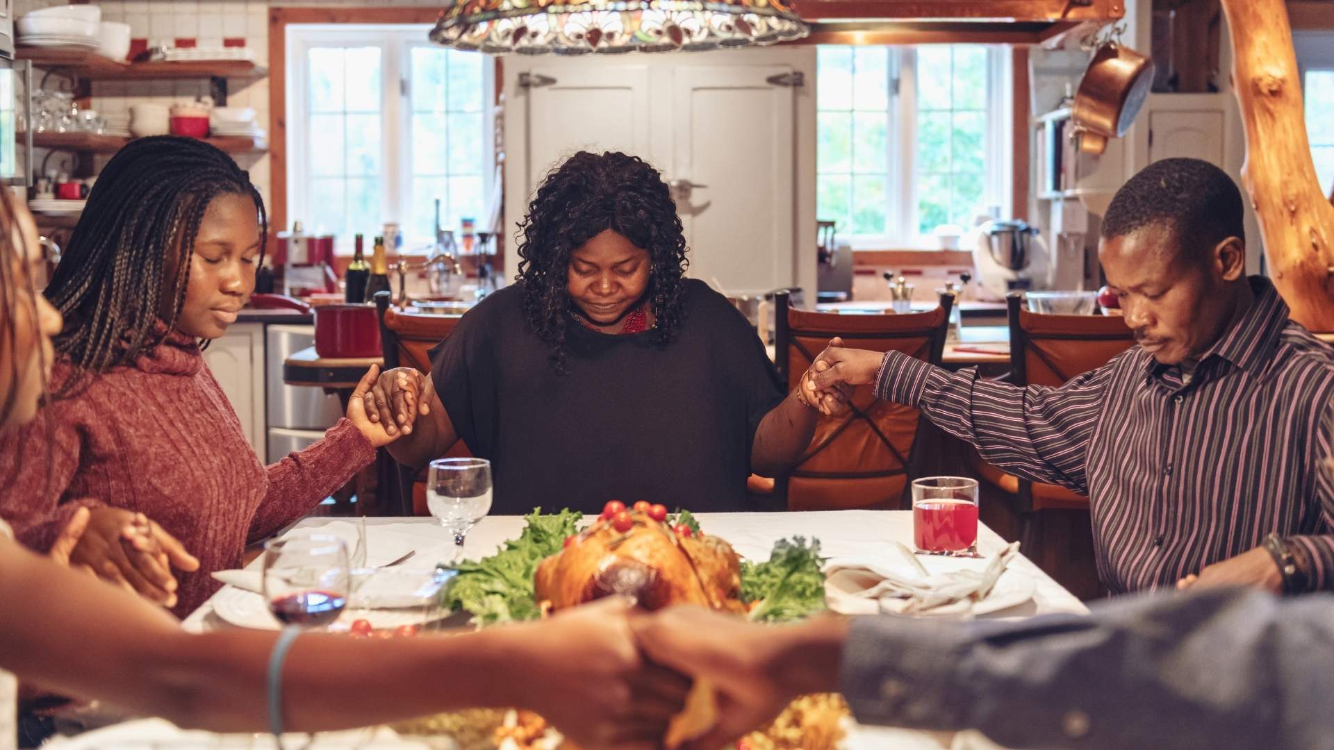 prayer happening around dinner table holding hands in pray