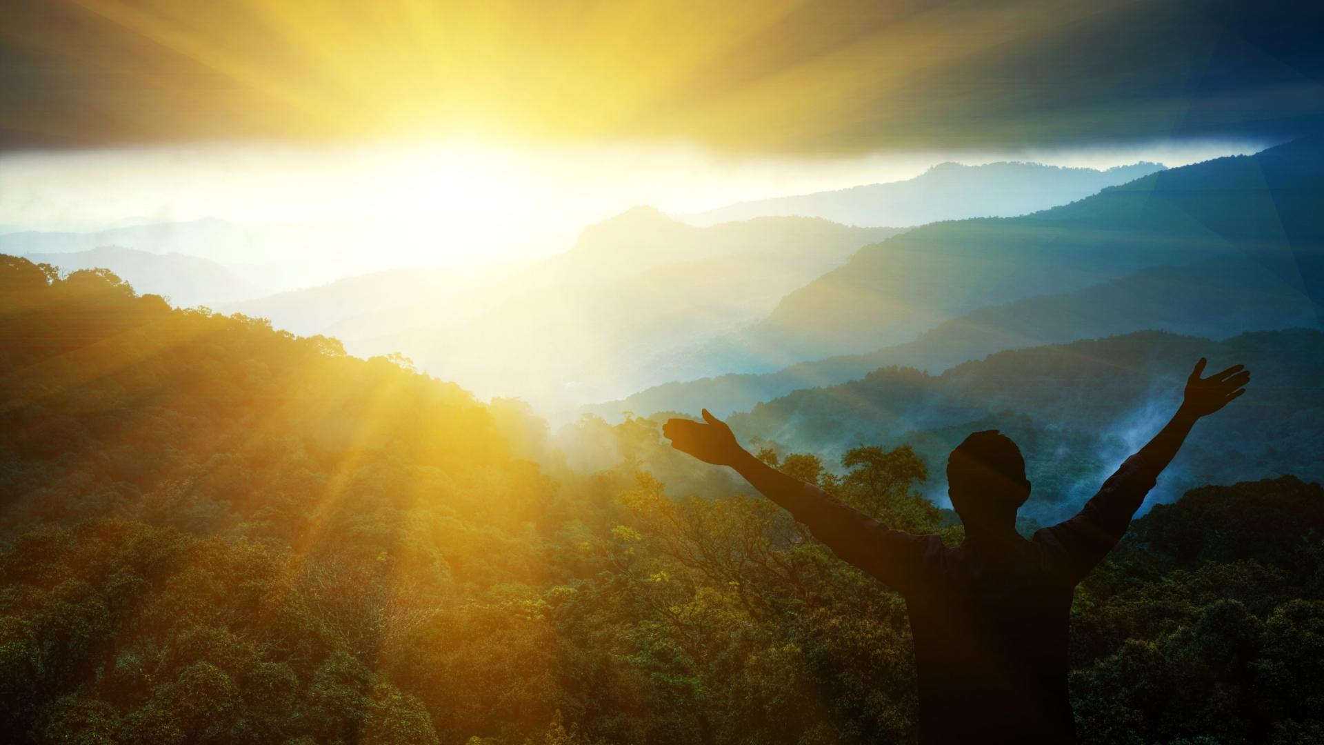 man praising the sun with his arms spread out accepting faith among a forest