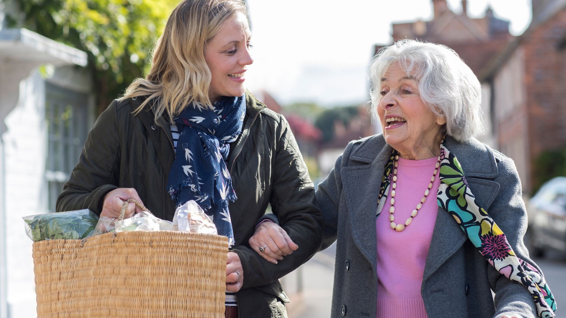 young woman helping older woman carry in woven basket of groceries